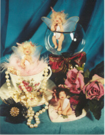 Three baby fairies, one in teacup, one in wineglass, one in front of roses