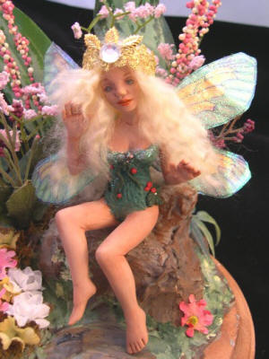 7 inch fairy doll made from polymer clay, faux cicada wings, sitting on a faux rock in a garden patch, with a gold crown